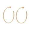 A pair of 2-inch gold-colored hammered hoop earrings made from recycled brass, viewed from a side angle against a white background.