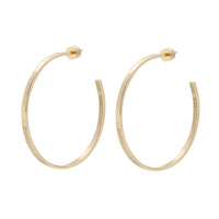 A pair of 2-inch gold-colored hammered hoop earrings made from recycled brass, viewed from a side angle against a white background.