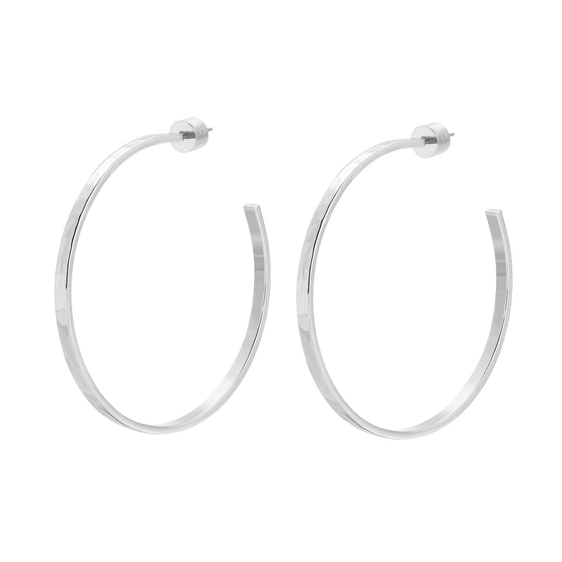 A pair of 2-inch gold-colored hammered hoop earrings made from recycled brass, viewed from a side angle against a white background.