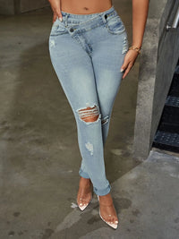 Person wearing light blue ripped jeans on a concrete floor.