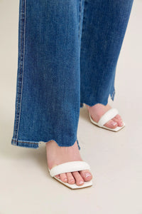 Person wearing blue jeans and white sandals on a light background