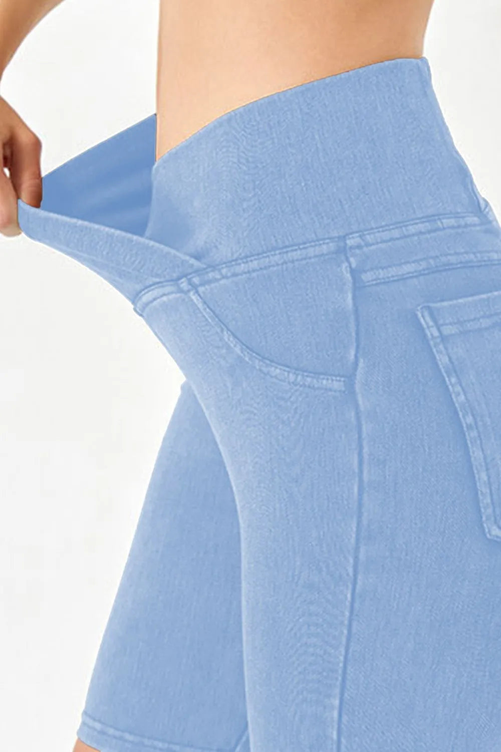 Light blue denim shorts being stretched by a hand on a white background