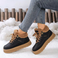 Black winter boots with brown fur and soles worn by a person in snow.