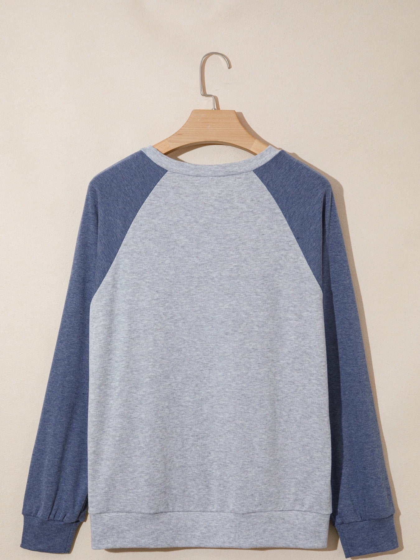 Gray and blue sweatshirt on a wooden hanger against a beige background