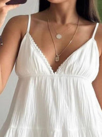 Woman wearing a white dress with thin straps and a gold necklace.