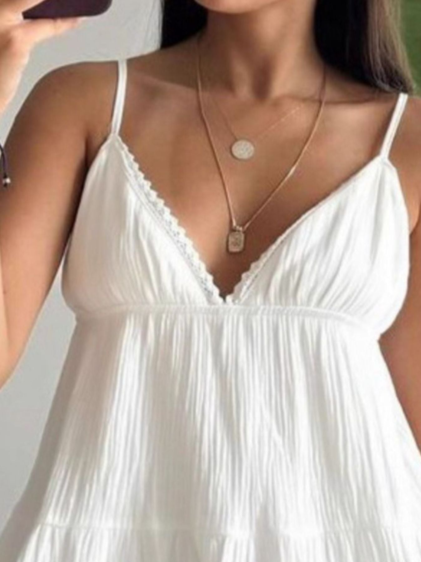 Woman wearing a white dress with thin straps and a gold necklace.