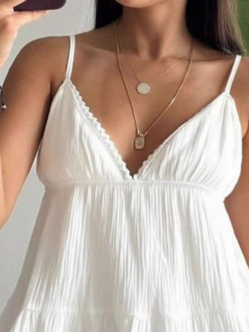 Woman wearing a white dress with thin straps and a gold necklace.