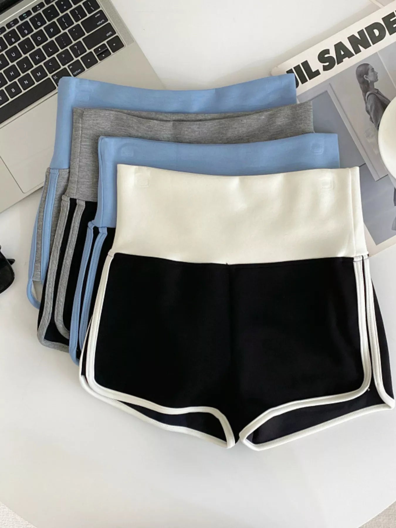 Four pairs of shorts in black, white, gray, and blue on a desk.