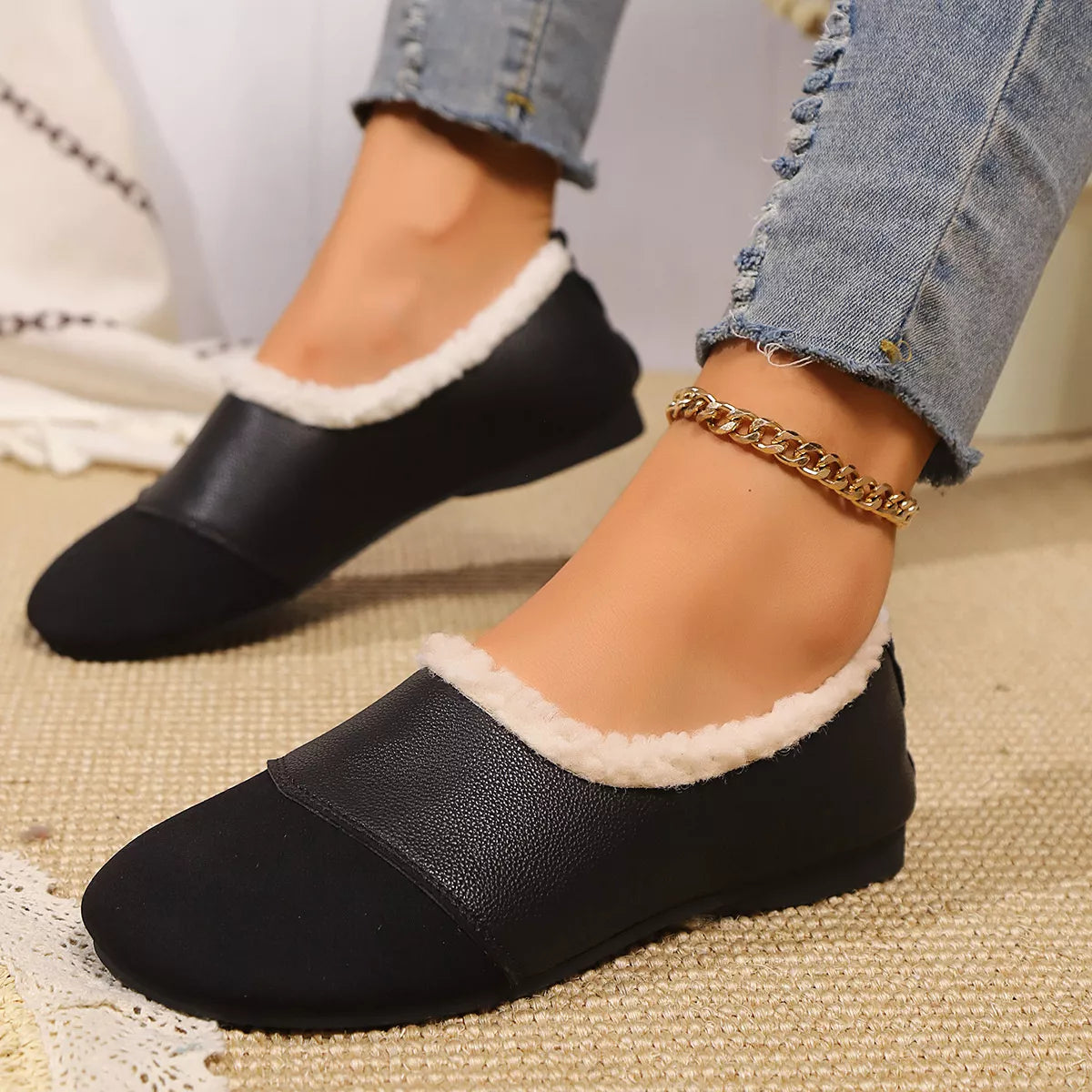Black slippers with white lining worn by a person on a textured surface.