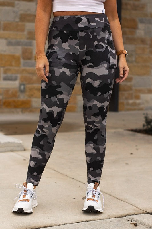 Person wearing camouflage leggings and white sneakers on a sidewalk.