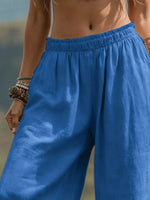 A close-up of a person wearing loose, wide-leg blue pants with an elastic waistband, shown outdoors against a blurred natural background.
