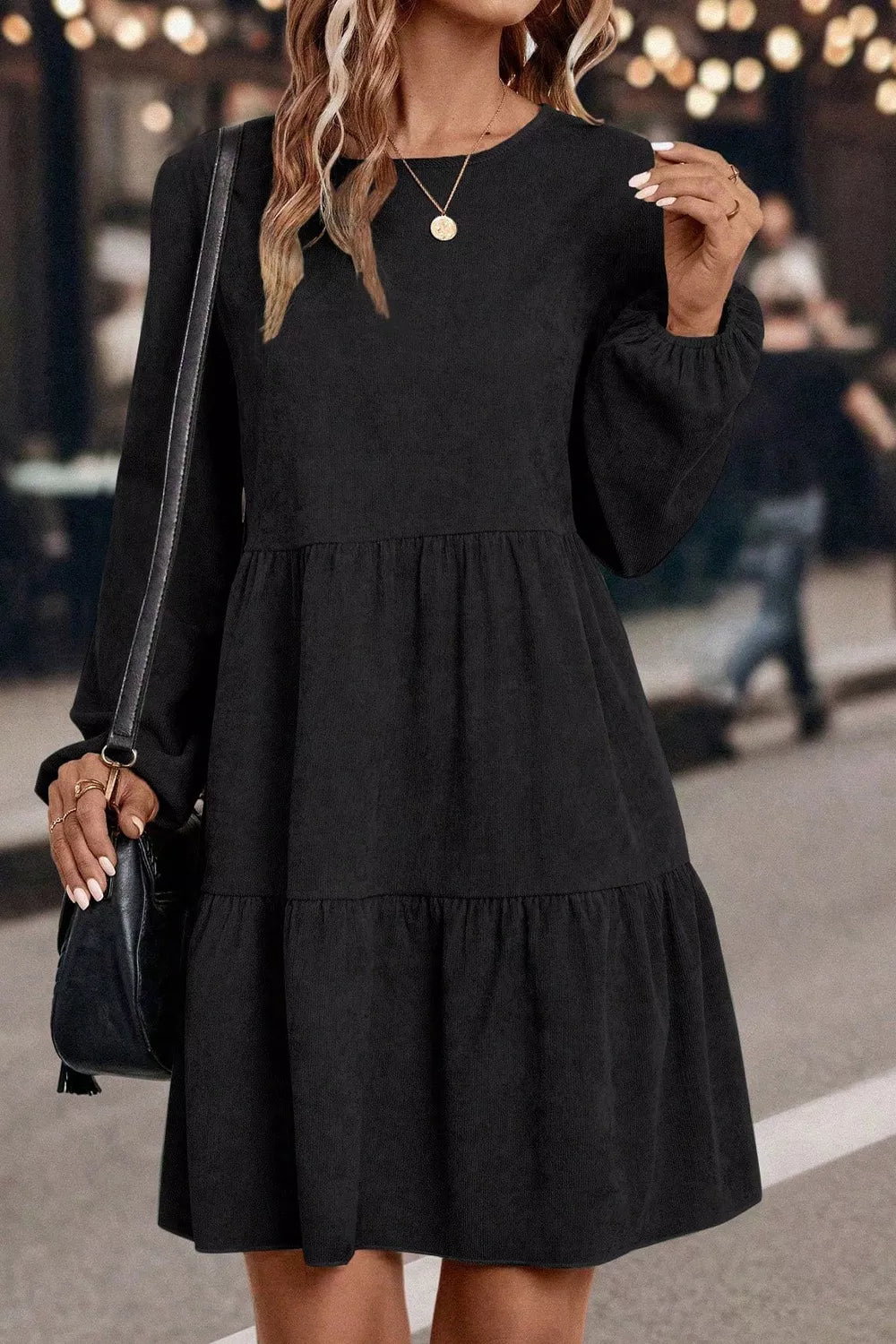 Woman wearing a black dress with long sleeves and a layered skirt, holding a black handbag.