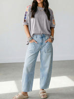 Person wearing a gray t-shirt with colorful sleeves and light blue jeans indoors.