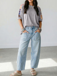 Person wearing a gray t-shirt with colorful sleeves and light blue jeans indoors.