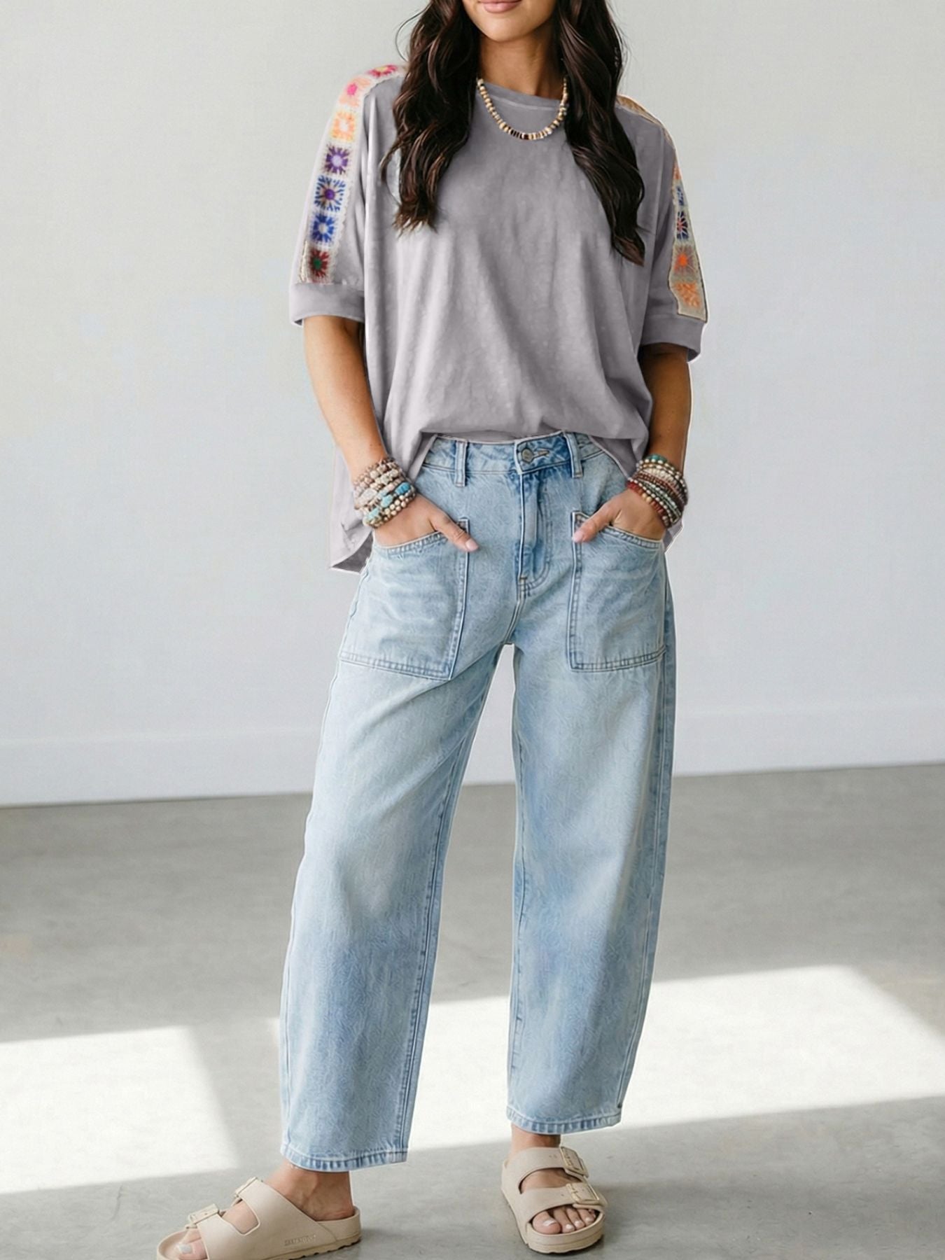 Person wearing a gray t-shirt with colorful sleeves and light blue jeans indoors.