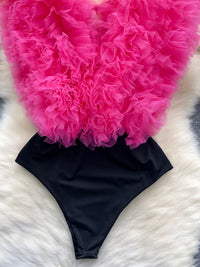 Black bikini bottom with pink ruffled fabric on a white and gray textured surface