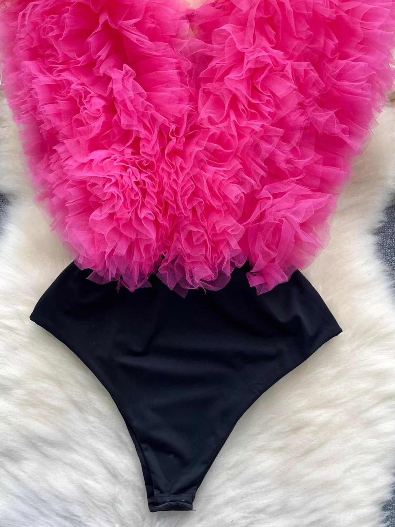 Black bikini bottom with pink ruffled fabric on a white and gray textured surface