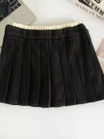 Black pleated skirt on a white surface with a laptop and magazine in the background.