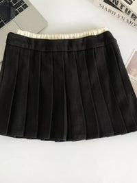 Black pleated skirt on a white surface with a laptop and magazine in the background.