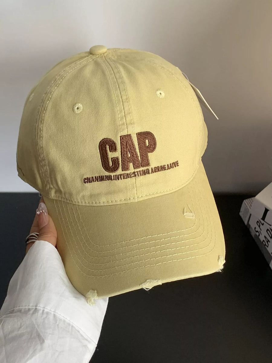 Beige cap with 'GAP' logo held by a person against a neutral background