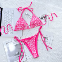 Pink leopard print bikini set on a white surface with magazines underneath