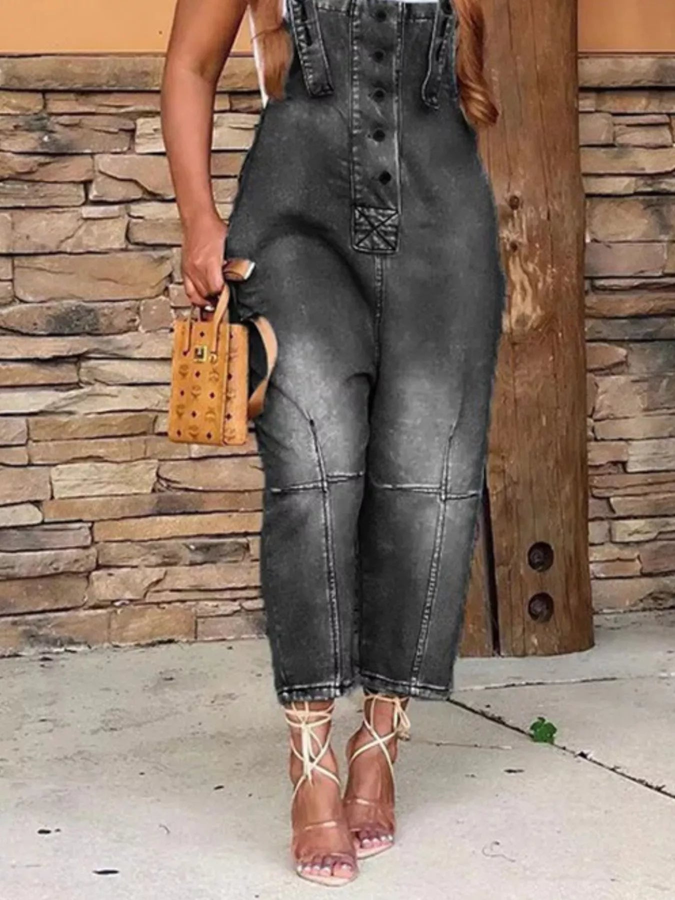 Person wearing black denim overalls standing against a stone wall.