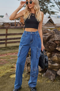 Woman wearing a black crop top and blue jeans standing near a stone wall outdoors.