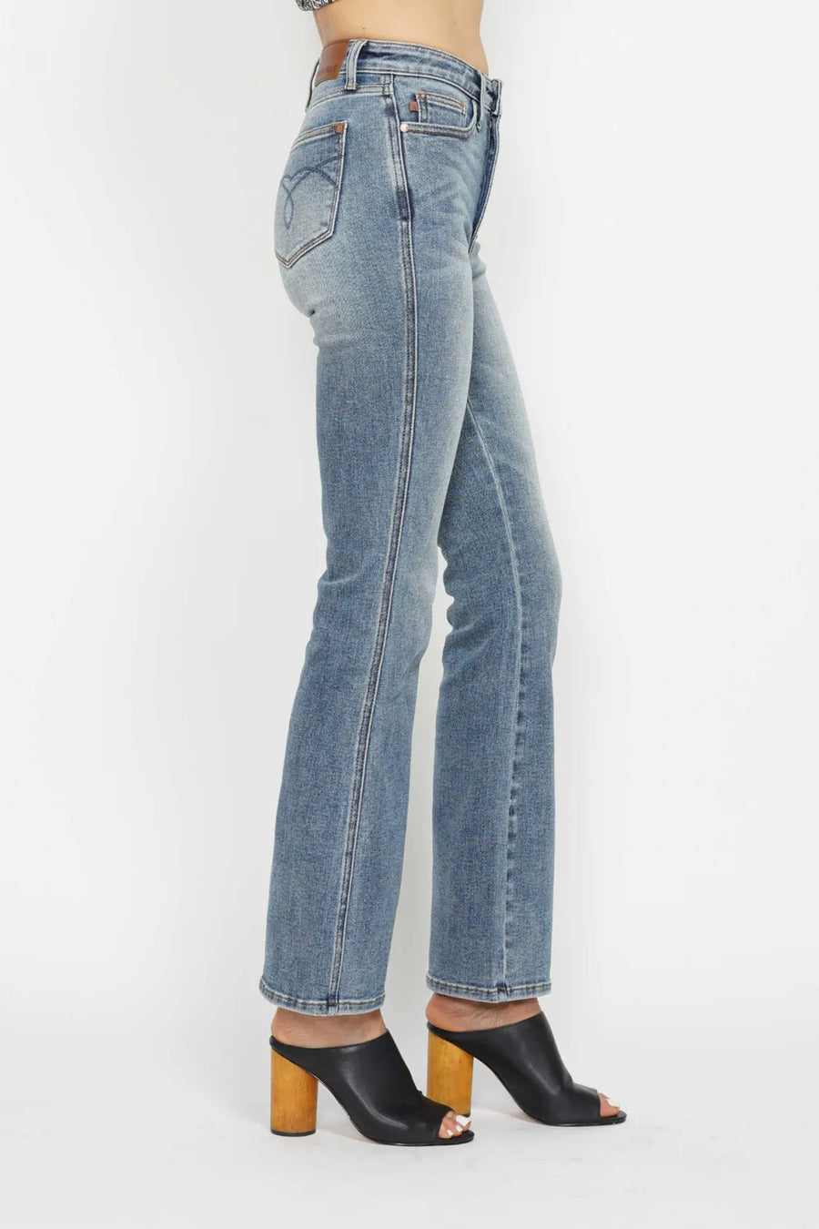 Person wearing light blue jeans and black open-toe shoes on a white background