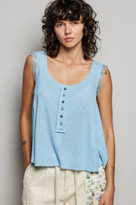 Woman wearing a light blue sleeveless top with lace trim on a plain background