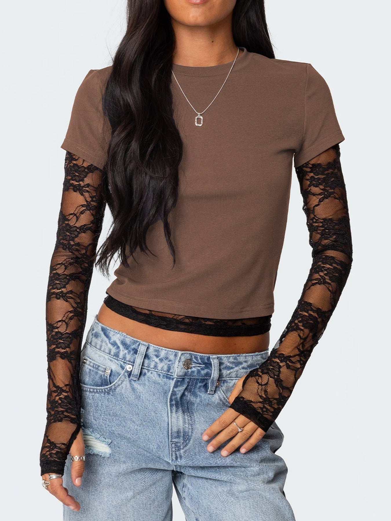 Person wearing a brown top with lace sleeves and blue jeans on a white background