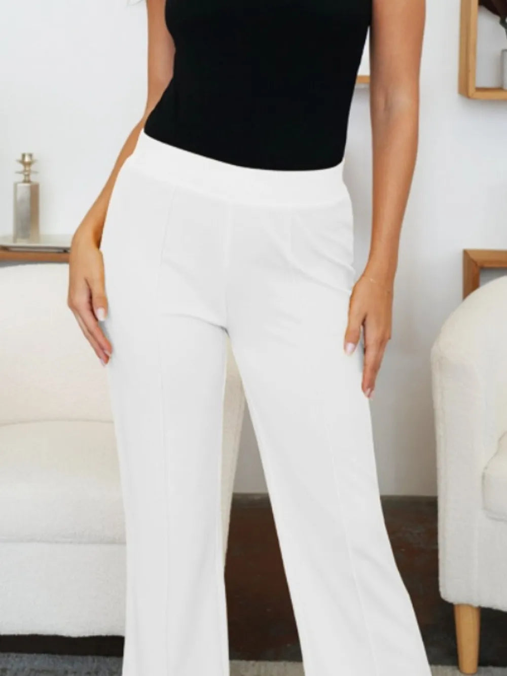 Person wearing white pants and a black top in a room with furniture.