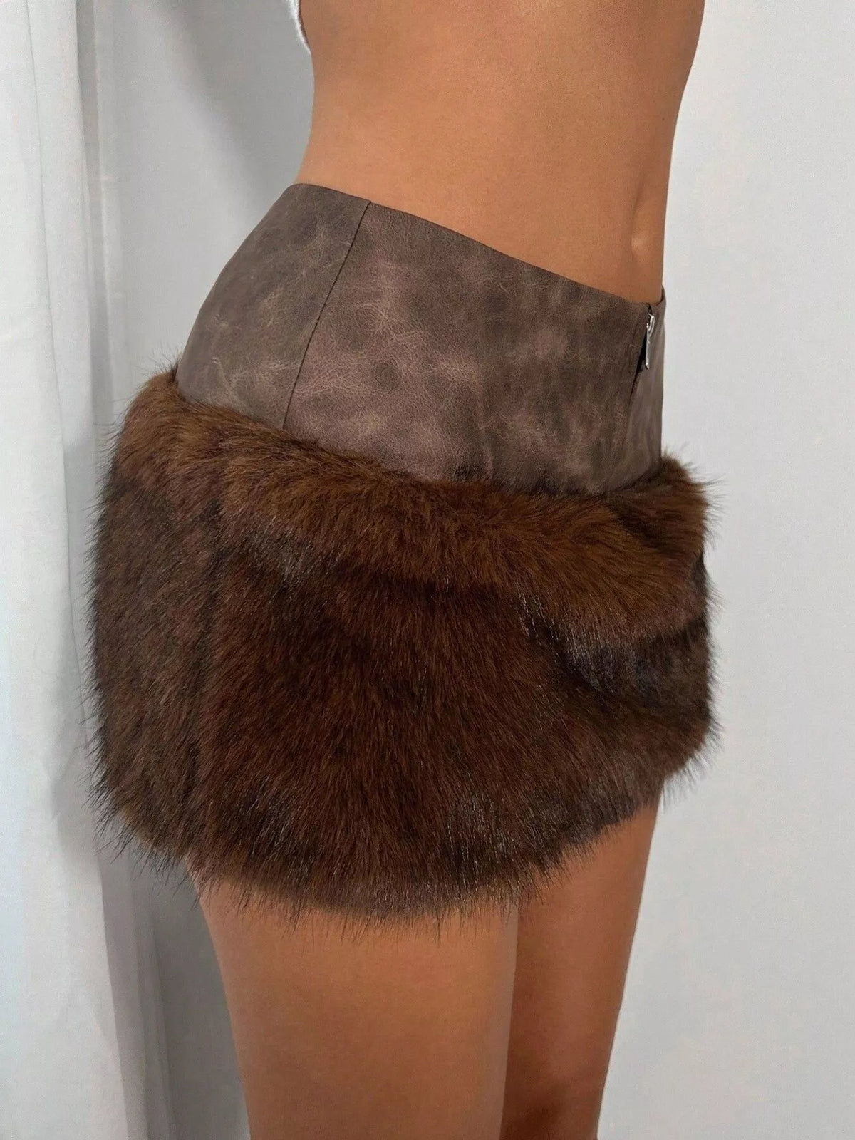 A close-up side view of a person wearing a brown faux-fur mini skirt with a taupe-brown faux-leather waistband and a small side zipper.
