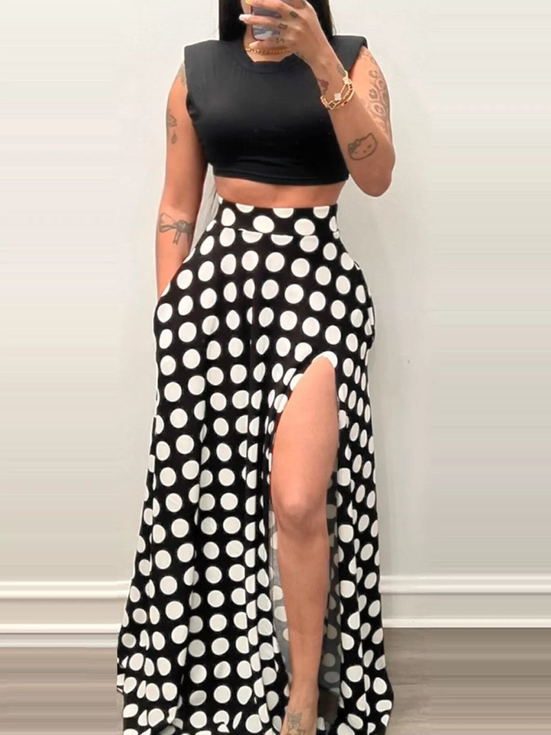 Person wearing a black crop top and polka dot pants with a high slit on a white background