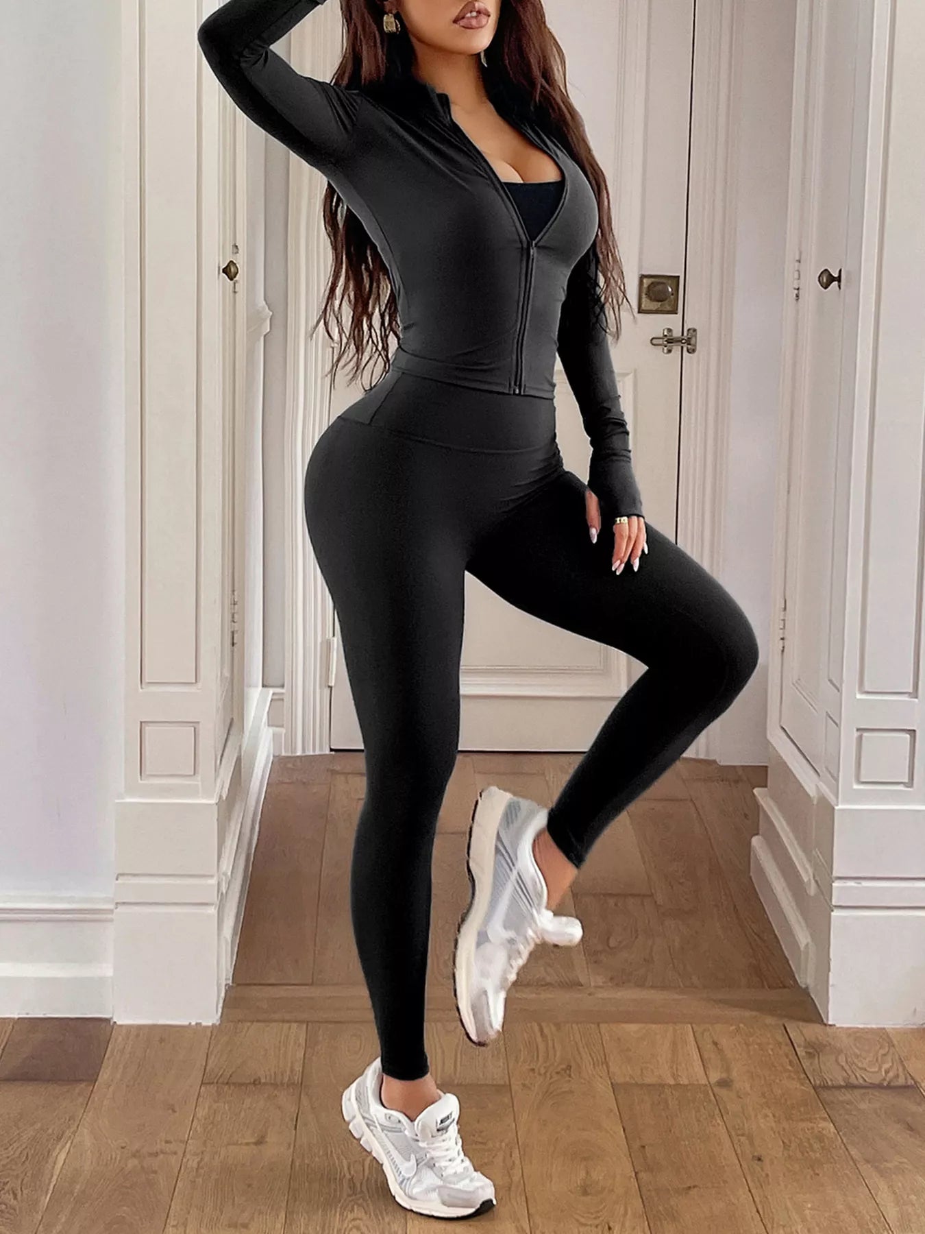 Woman wearing a black athletic outfit with white sneakers in an indoor setting.