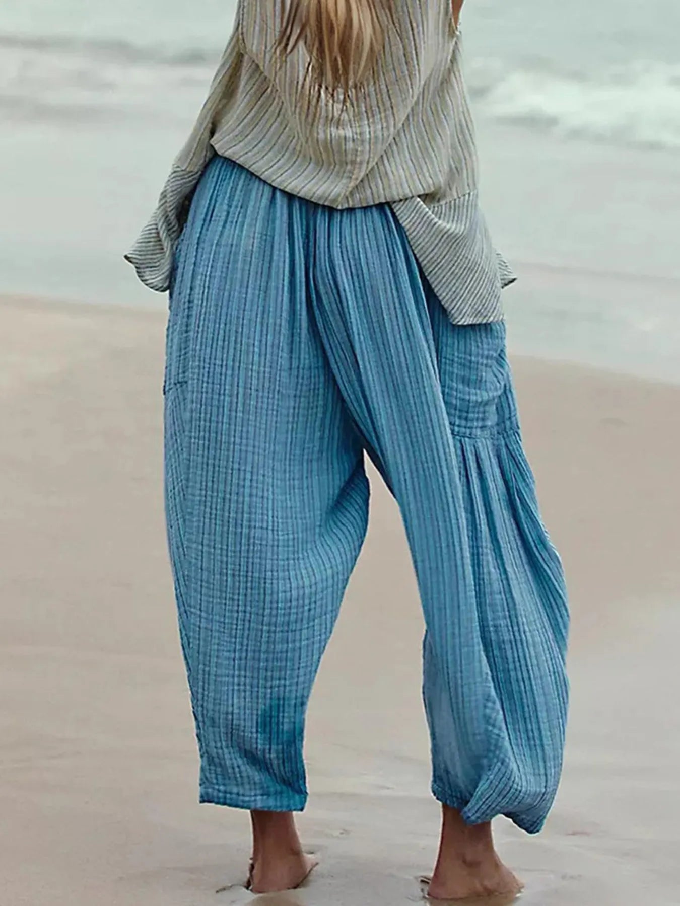 Person wearing blue checkered pants and a striped shirt on a beach.
