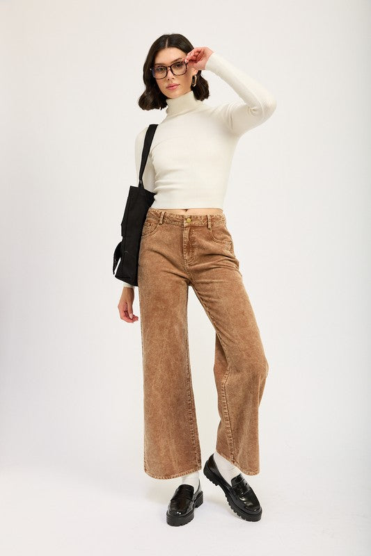 Woman wearing a white turtleneck, brown wide-leg jeans, and black shoes on a white background