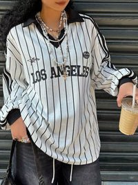 Person wearing a 'Los Angeles' striped shirt holding a drink.