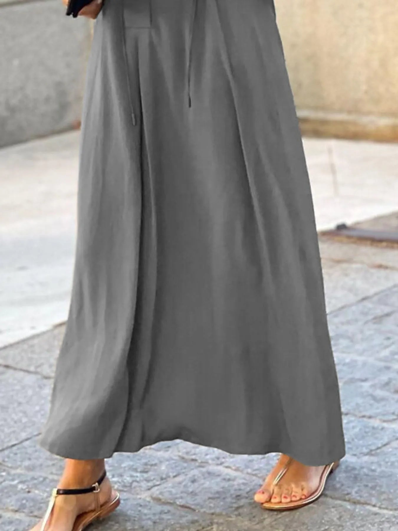 Gray wide-leg pants worn by a person on a stone pavement.