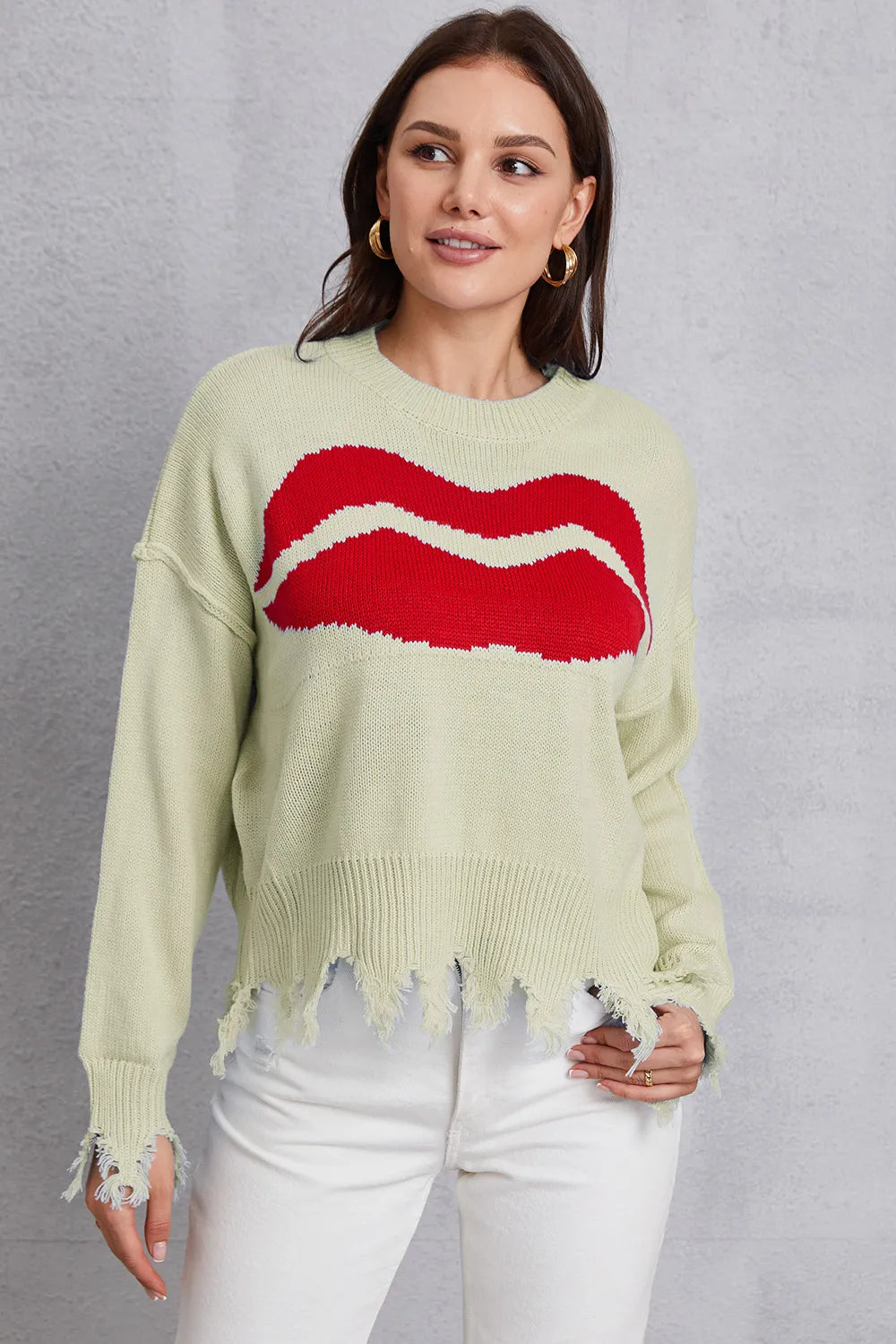 Woman wearing a light green sweater with a red graphic design on a gray background