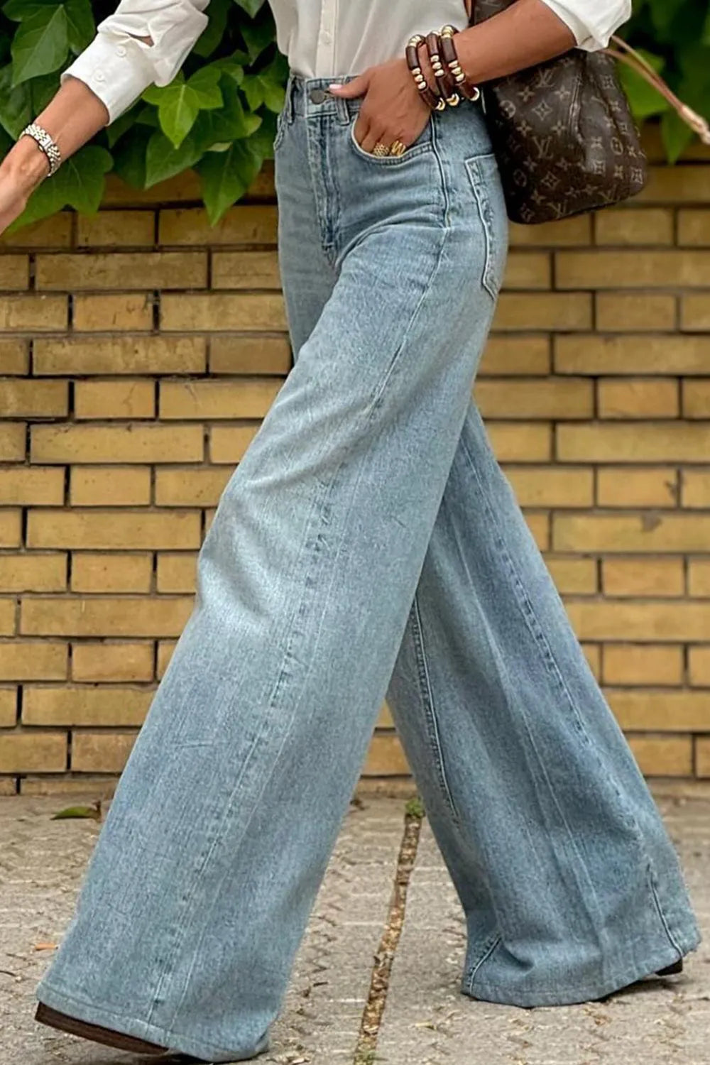 Person wearing light blue wide-leg jeans with a brick wall background