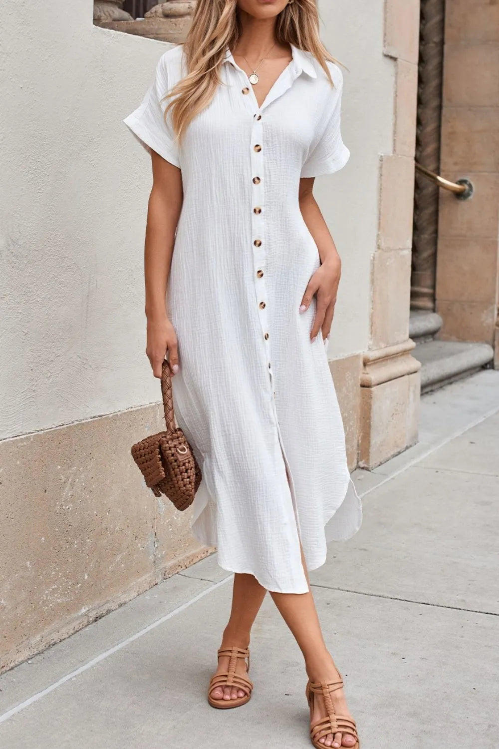 Woman wearing a white dress with a textured pattern, standing against a beige wall.