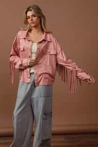 Woman wearing a pink fringed jacket and gray pants against a brown background