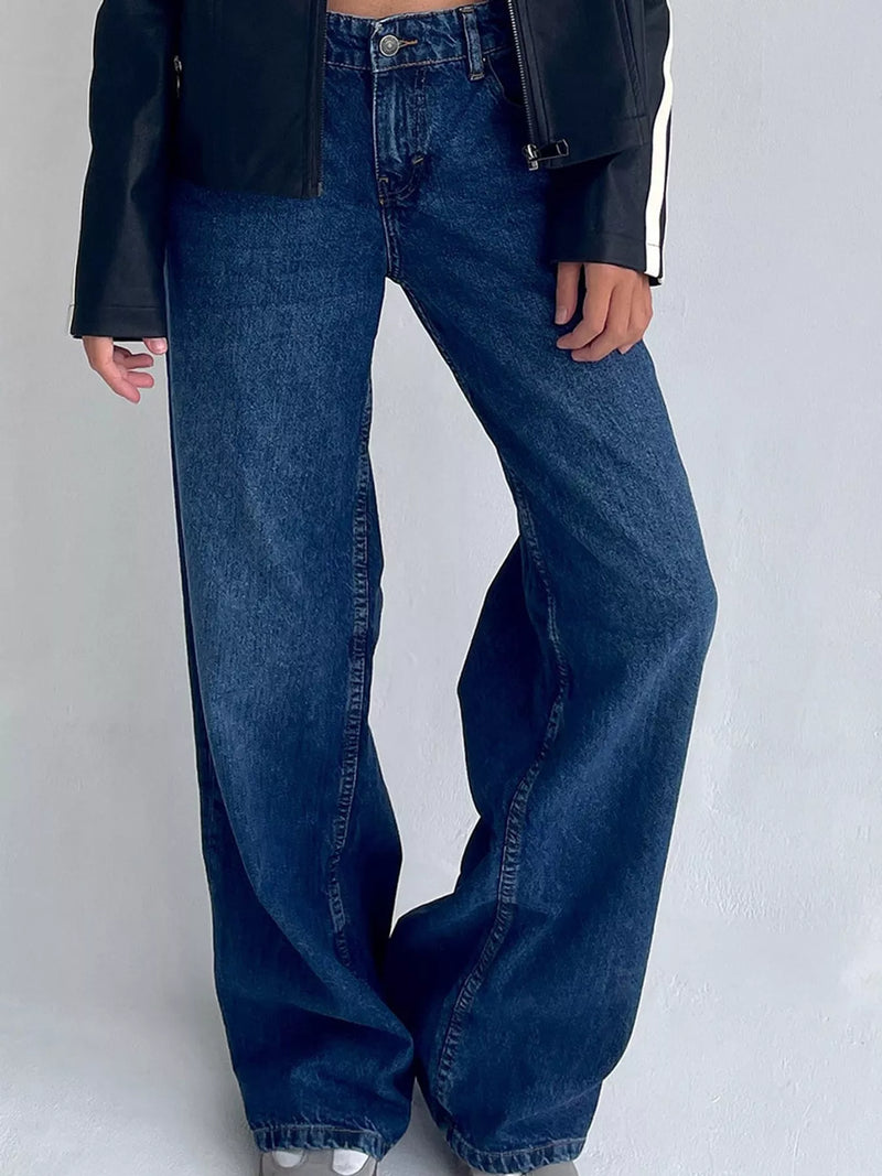 A person wearing dark blue wide-leg denim jeans with a black jacket featuring white side stripes, shown from the waist down against a light gray studio background.