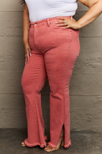 Person wearing coral pink jeans with a white top against a neutral wall.
