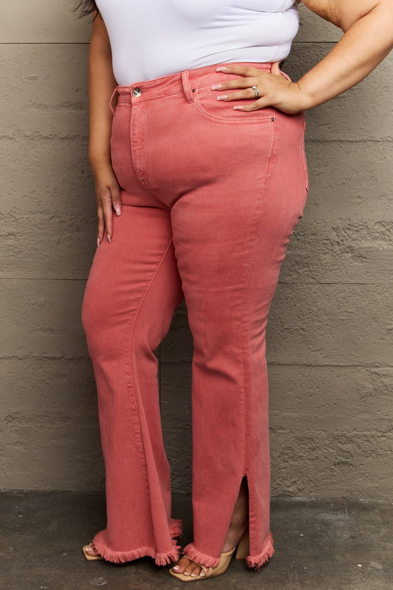 Person wearing coral pink jeans with a white top against a neutral wall.