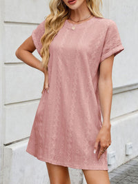 Woman wearing a pink lace dress against a white wall.