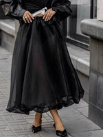 Person wearing a black dress with sheer overlay on a city street.