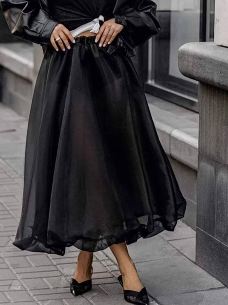 Person wearing a black dress with sheer overlay on a city street.