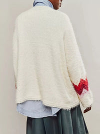 Person wearing a cream-colored sweater with red floral patterns on sleeves against a plain background