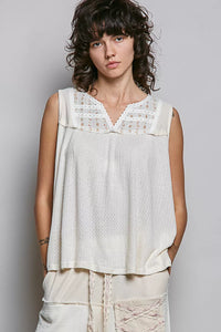 Woman wearing a sleeveless top with lace details against a plain background